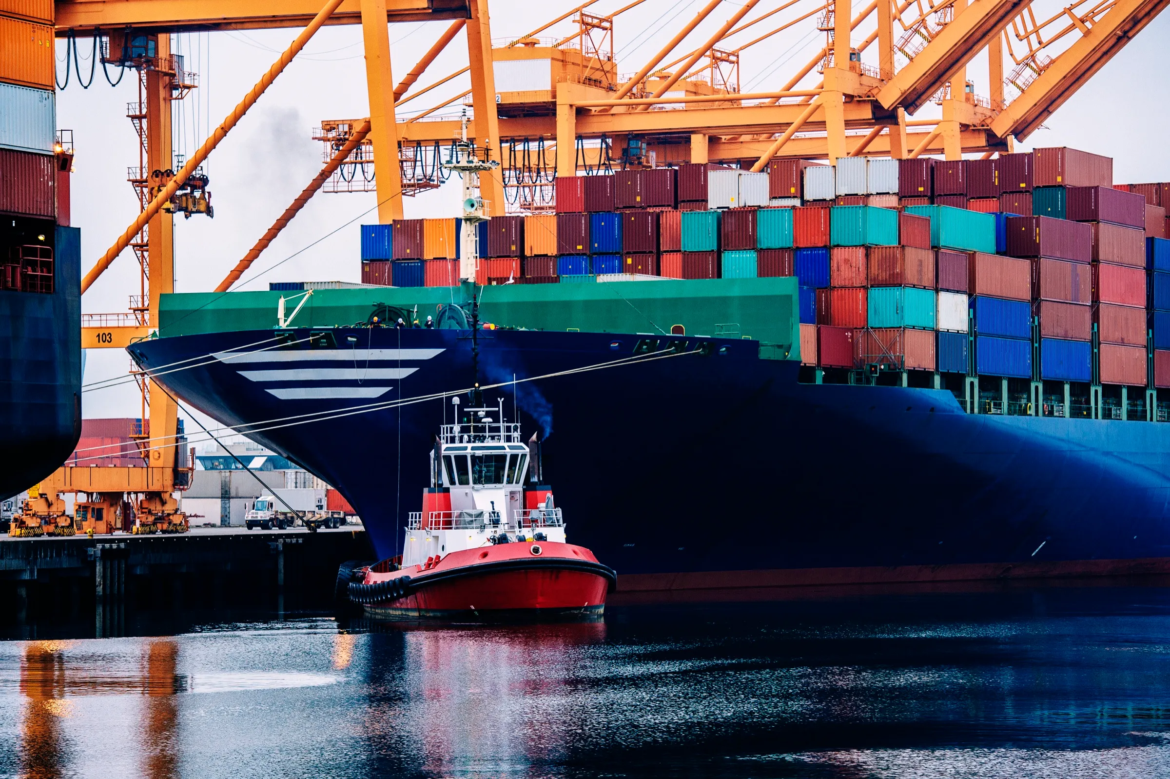 Tugboat alongside a container vessel arriving at berth