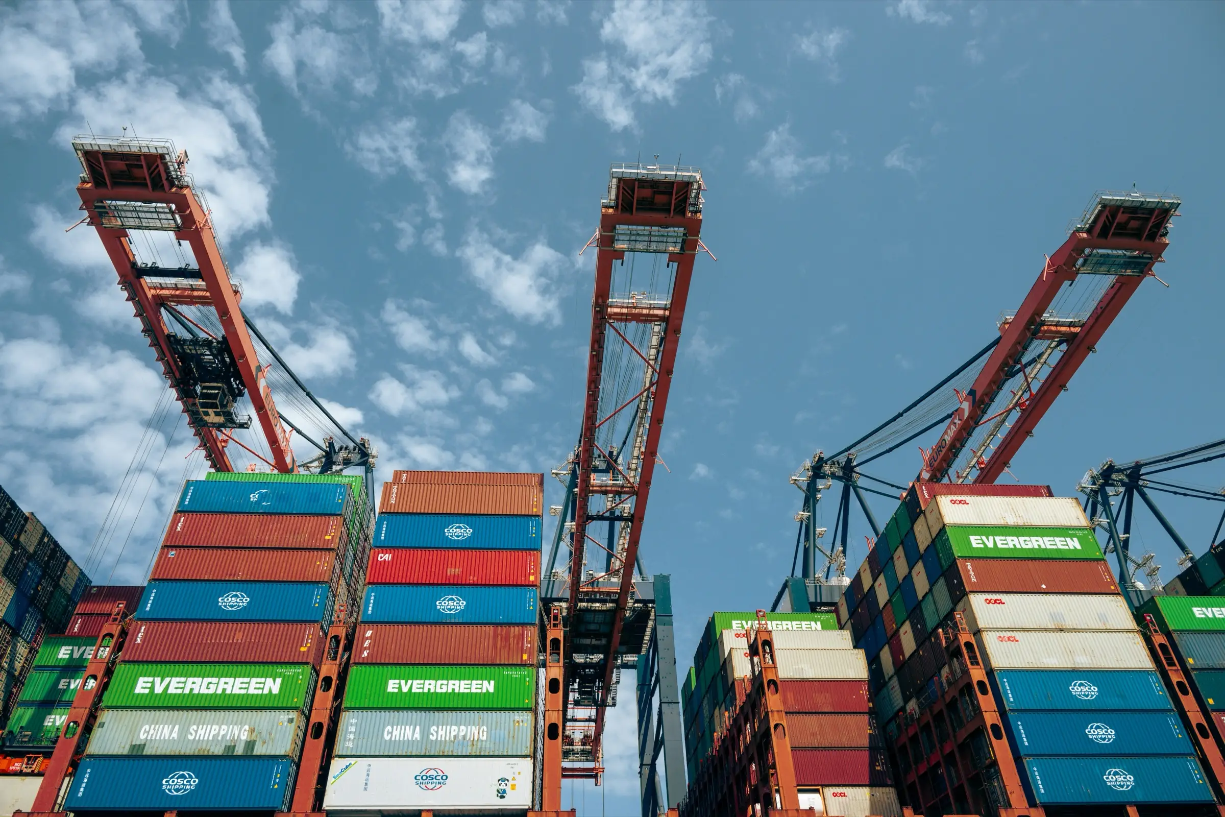 Ship-to-shore gantry cranes above stacked containers against a blue sky