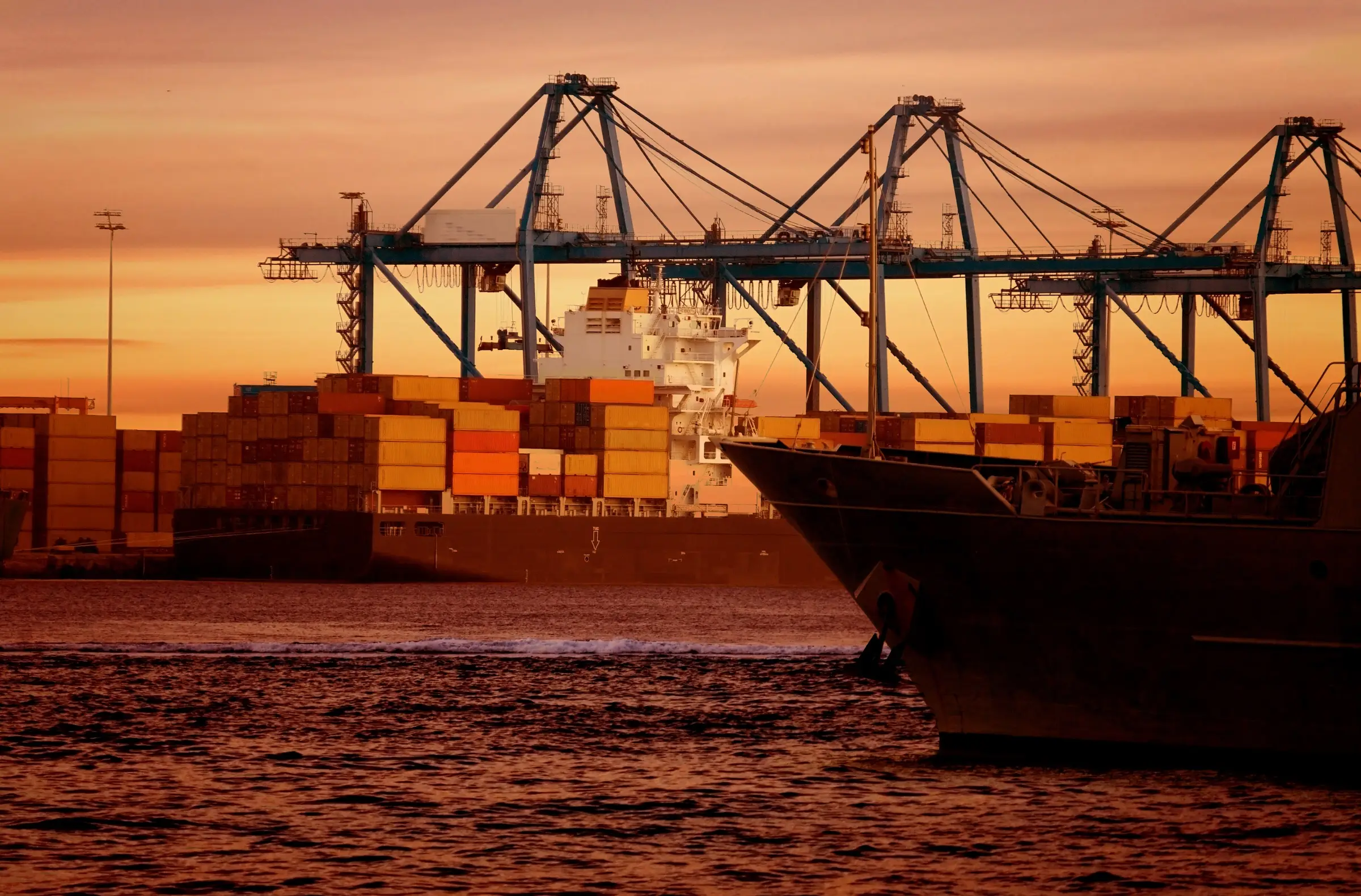 Cargo vessel and container cranes silhouetted at sunset